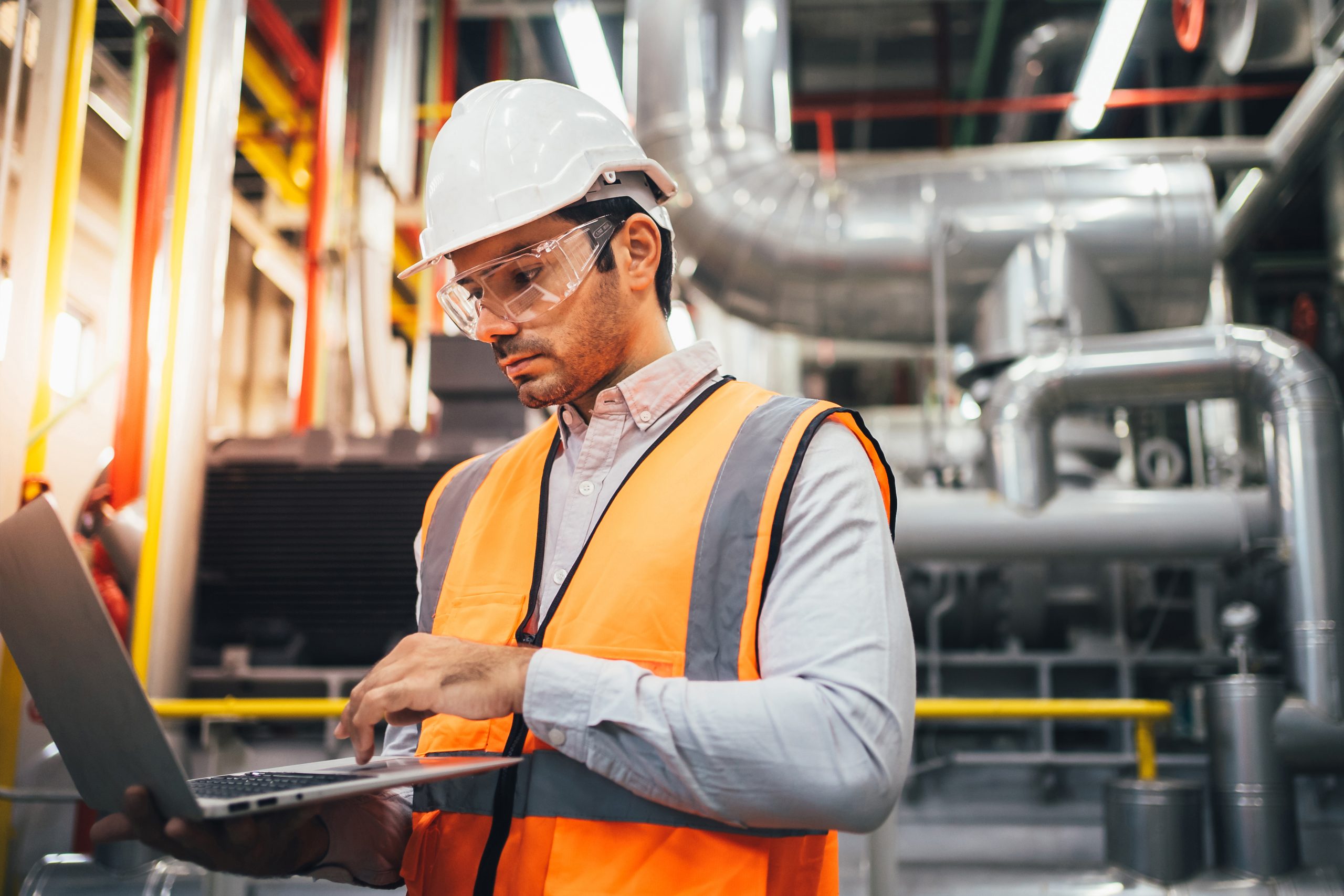 Portrait of engineer technician using laptop controlling machine and working at industrial plant factory