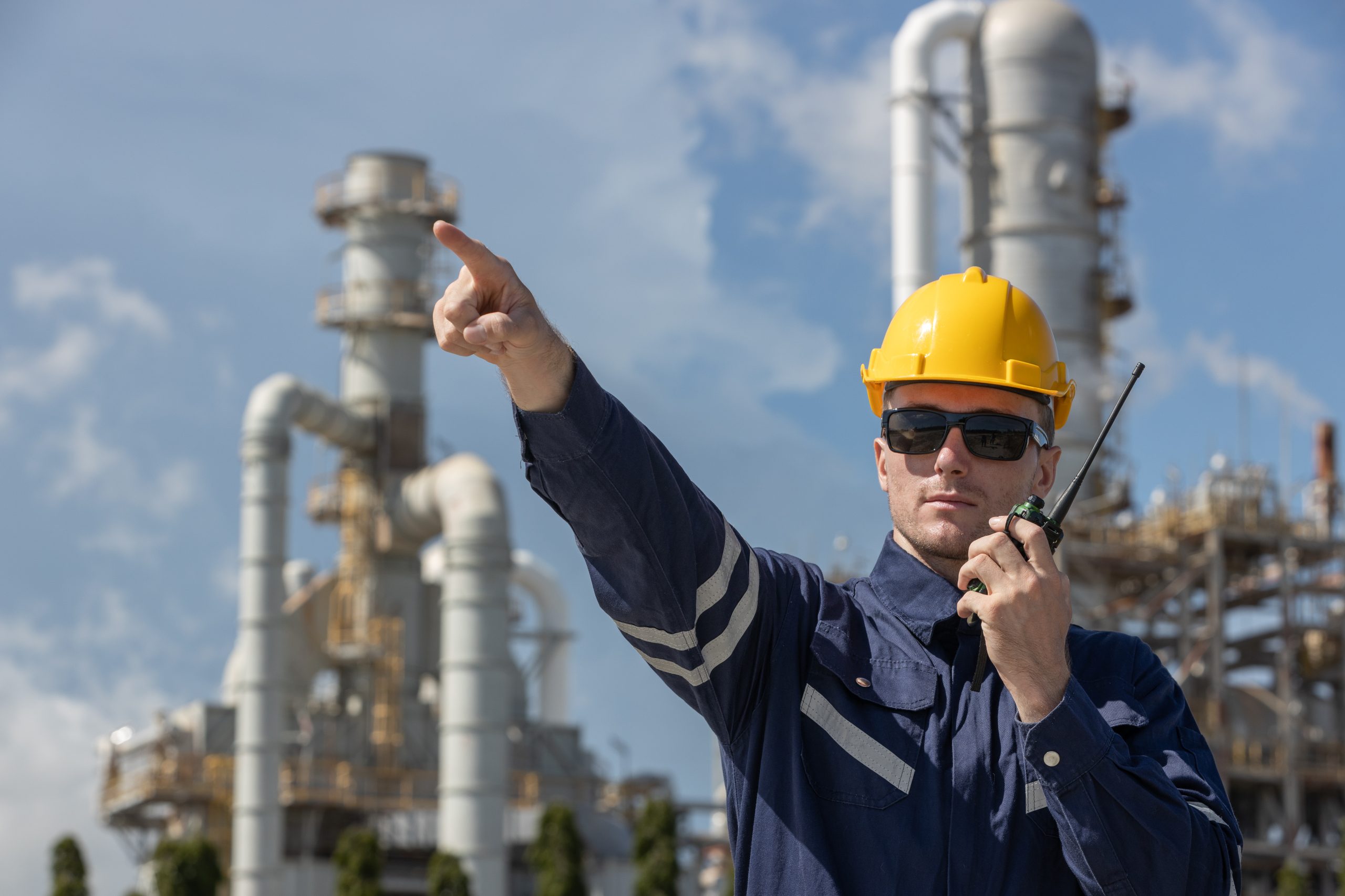 Man professional engineer technician wear safety uniform and white hard hat working area near tank refining oil petrochemical industry factory. Industrial factory site energy power station.